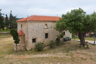 A historic stone building in a rural setting with a large tree, Metochi of the Monastery of St