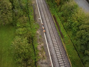 Aerial view of workers working and walking on a railway line through a forest, tamping machine,