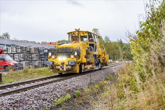 Rail vehicle on tracks in industrial environment with cloudy sky, tamping machine, Hermann