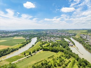 Hilly landscape with wide fields and a meandering river under a blue sky, with a small village on