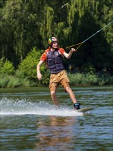 Young casual man with flapping shirt on wakeboard in lake, water ski and wakepark, Stráž pod