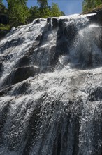 A high waterfall flowing over rocks and falling into the depths, in sunny weather and surrounded by