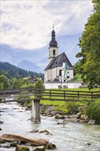 Parish church of St Sebastian by a river in an idyllic Alpine landscape with mountains and forests