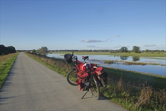 Red loaded bicycle on a road next to a wide landscape with water and sky, bicycle tourism,