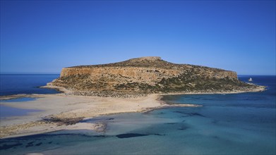 Aerial view of a large, rocky island with a steep coastline surrounded by blue water, Gramvoussa,