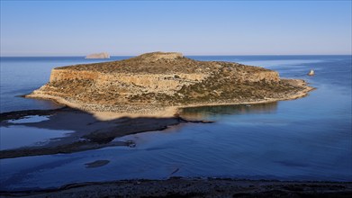 Island surrounded by calm sea with rocky cliffs, under clear day skies, natural beauty, Gramvoussa,