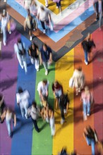 People crossing a pedestrian crossing, on a road, the road surface is colourful, in rainbow