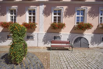 Facade of a house with windows and flower boxes with blooming geraniums, bench, planter with a