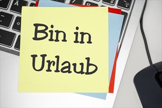 Notepad with the inscription BIN IN URLAUB on a laptop