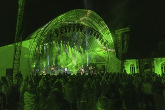 Large crowd at a night-time concert in front of a green-lit stage, Klostersommer, Calw Hirsau,