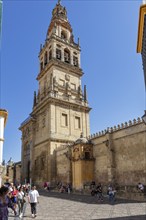 High bell tower of a historic building with people and blue sky as background, Cordoba