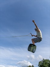 Young man jumping and flying with wakeboard, water sports and water skiing in the wakepark