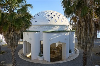 White dome-shaped structure surrounded by palm trees with decorative elements and stepped entrance,