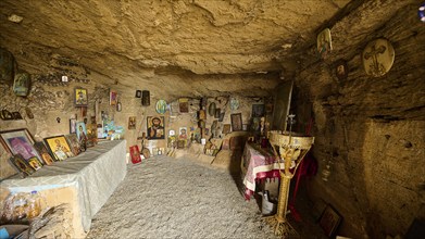 Interior view of a rock cave, with religious icons on the walls and a decorative table creating a