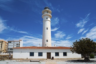 White lighthouse with neighbouring building under blue sky with clouds, sunny atmosphere, Faro de