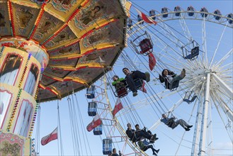 People swinging on a carousel in front of a Ferris wheel in sunny weather at a funfair, Europa Rad,