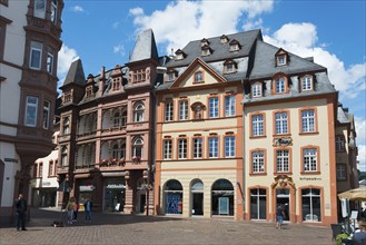 Multi-storey historic buildings with red facades and shutters surround a lively town square,