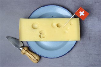 A piece of Swiss Emmental cheese on a plate and the Swiss flag