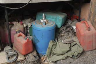 Old and dusty empty red plastic gas canisters, blue water containers and boots stored underneath a