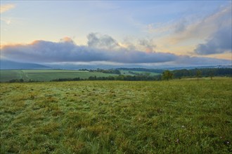 Green meadow and hills under a cloudy morning sky with a peaceful atmosphere, autumn, Eichelsbach,