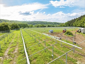 Installation of a solar park frame in a rural area, surrounded by green meadows and forests under a