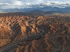 River bed runs through a landscape of eroded hills, badlands at sunset, mountain peaks of the Tian