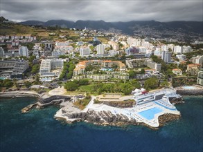 Aerial drone view of Funchal city with hotels resorts and swimming pool along the coast of Atlantic