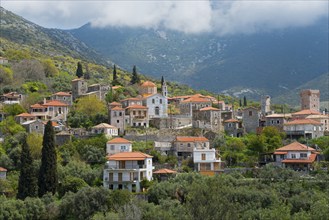 A traditional village with red roofs and a church tower, nestled in a green mountain landscape