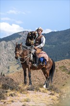 Traditional Kyrgyz eagle hunter with eagle in the mountains, hunting on horseback in front of dry