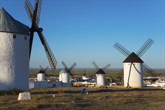 Several windmills on a grassy hill above a cityscape under a clear blue sky, windmills, Campo de