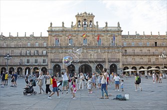 Street artists and children playing in the Plaza Mayor, behind the town hall, Salamanca, province