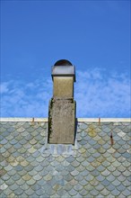 A stone chimney on a shingle-covered roof against a clear blue sky, Bergen, Vestland, Norway,