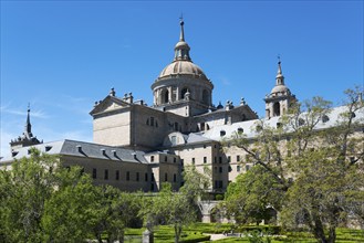 Impressive historic monastery with towers and domes surrounded by green trees under a blue sky,