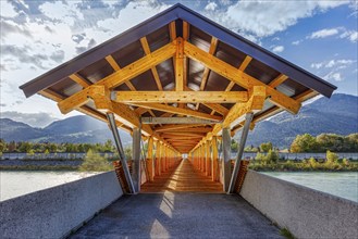 Wooden bridge with roof, flooded with sunlight, with mountain backdrop and river, Inn footbridge,