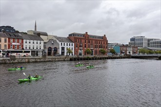 People paddling in kayaks on a river with industrial buildings in the background, Cork