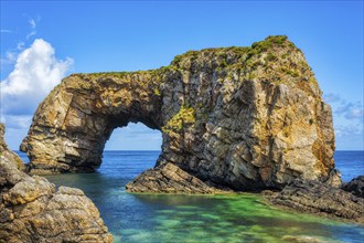 Large rock formation in the sea under a clear blue sky and sunshine, Great Pollet Sea Arch