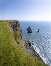 Steep coast, view from steep cliff to the rocks Reynisdrangar in the water, at Reynisfjara beach,