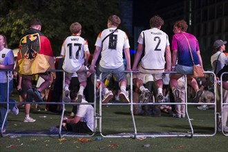 Fans with shirts of the German national team sit on barriers at the fan zone at the Brandenburg Tor