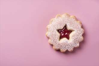 Top view of single traditional Linzer cookie with red fruit jam on pink background with copy space.