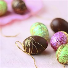 Small chocolate Easter eggs wrapped in shiny foil, placed on a bed of shredded pastel-colored