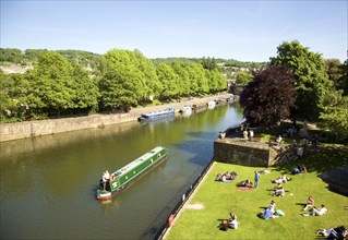 Narrow boats on River Avon and people in Parade Gardens, Bath, Somerset, England, UK