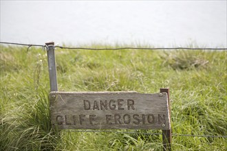 A wooden sign warning of the danger of cliff erosion at the top of the sheer cliffs at Beachy Head,