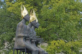 Sculpture Enthroned by Volkmar Kühn 2021, three bishops with golden mitres sitting on stool, row,