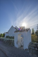 Whitewashed church in Dalby, backlight, stone wall made of boulders, entrance gate, Fyn, North