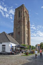 Tourists at sidewalk café and 13th century Gothic bell tower of Our Lady's Church in the village