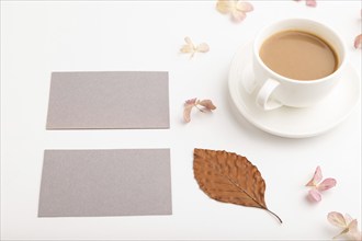 Composition with gray paper business card, brown beech autumn leaves, hydrangea flowers and cup of