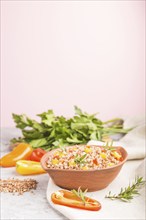 Buckwheat porridge with vegetables in clay bowl on a gray and pink background and linen textile.