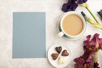 Blue paper sheet with cup of cioffee, chocolate candies, purple and burgundy iris flowers on gray