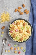 Millet porridge with candied fruits and almonds in blue ceramic bowl on a gray concrete background