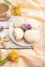 Meringues cakes with cup of coffee on a white wooden background and orange linen textile. Side